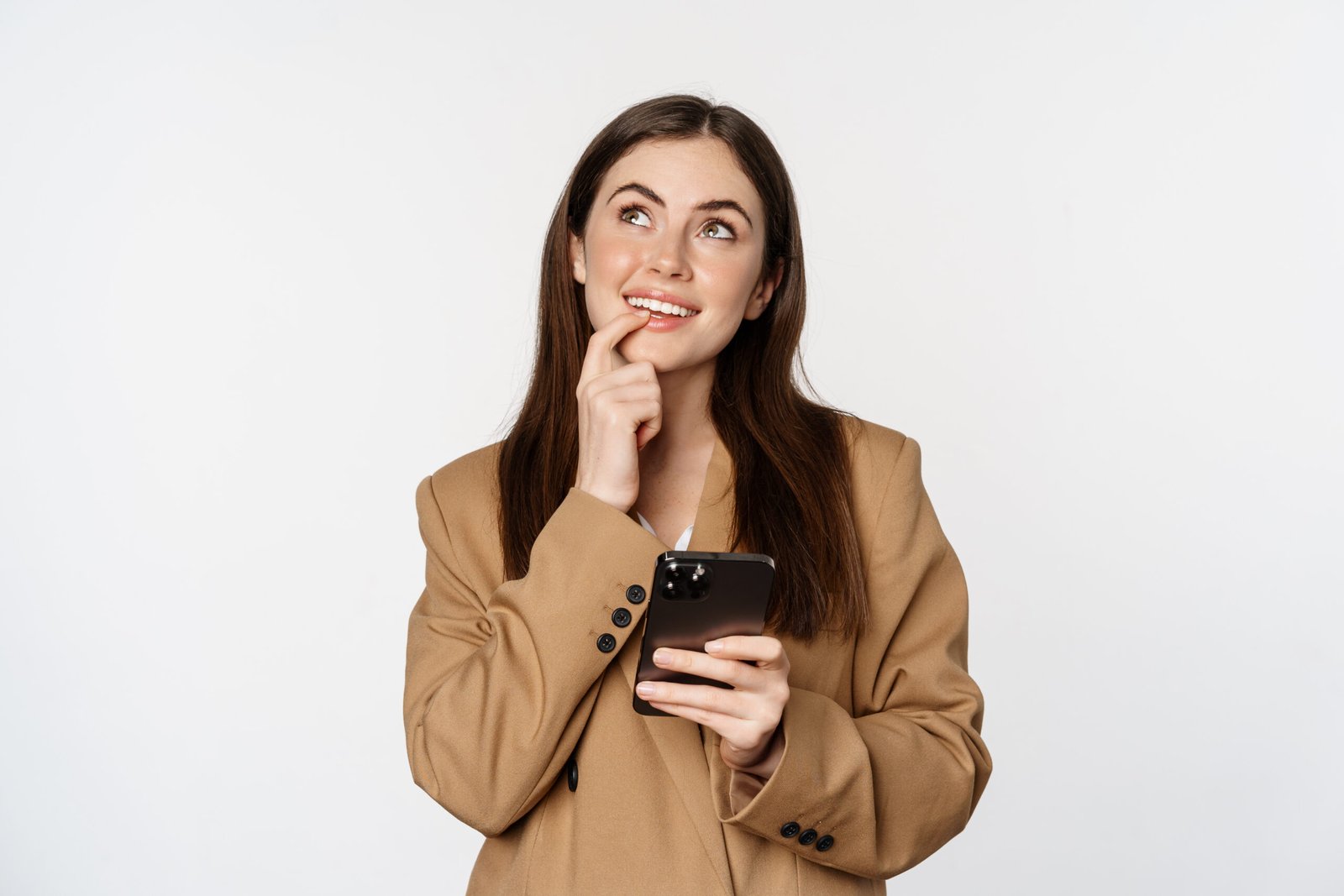 Image of businesswoman smiling, using mobile phone and thinking, making choice in smartphone app, standing against white background