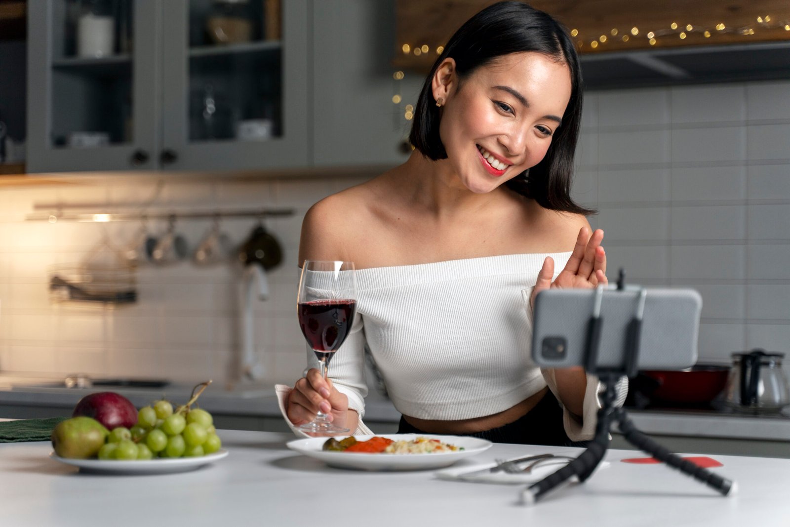 beautiful woman sitting down with wine on her right hand while making video with her phone in front of her