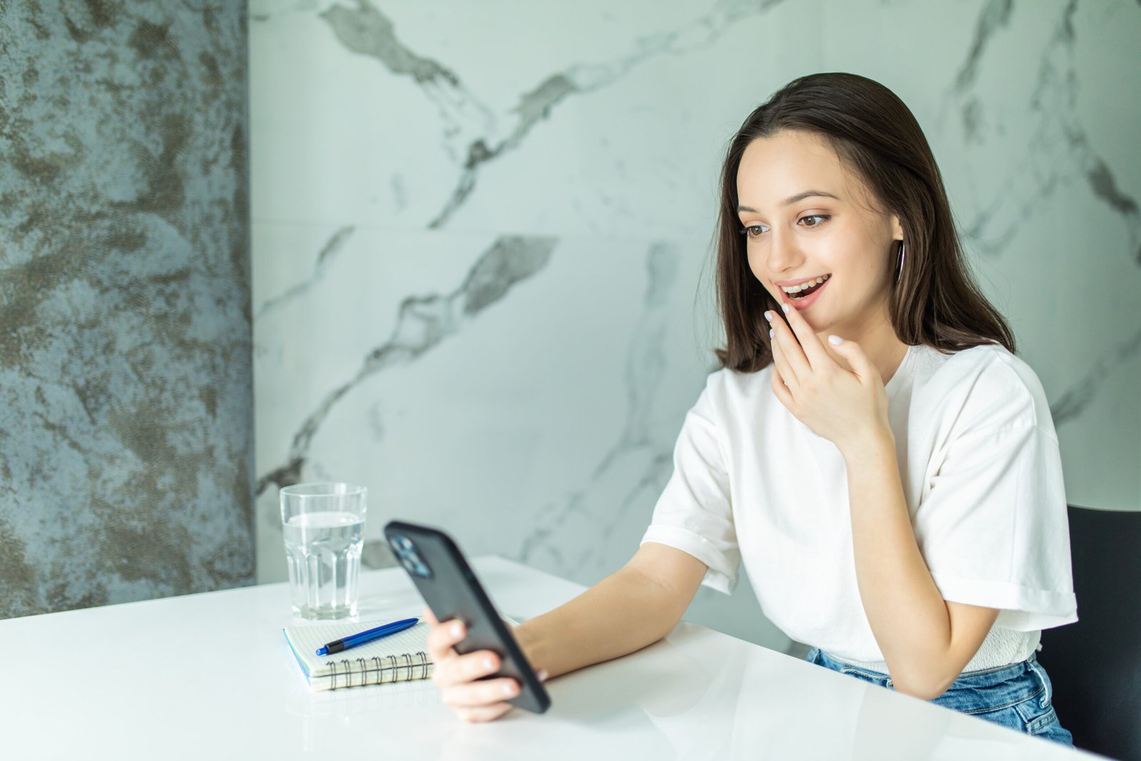 Smiling young woman using smart phone in kitchen. Woman scroll through the social network